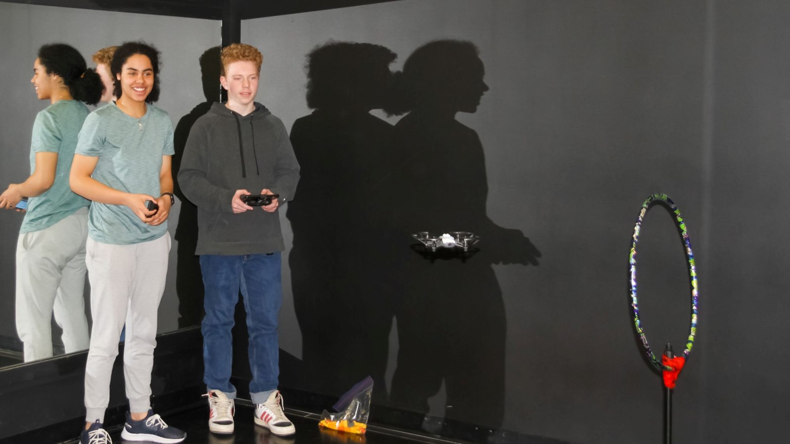Two students flying a drone through a hula hoop